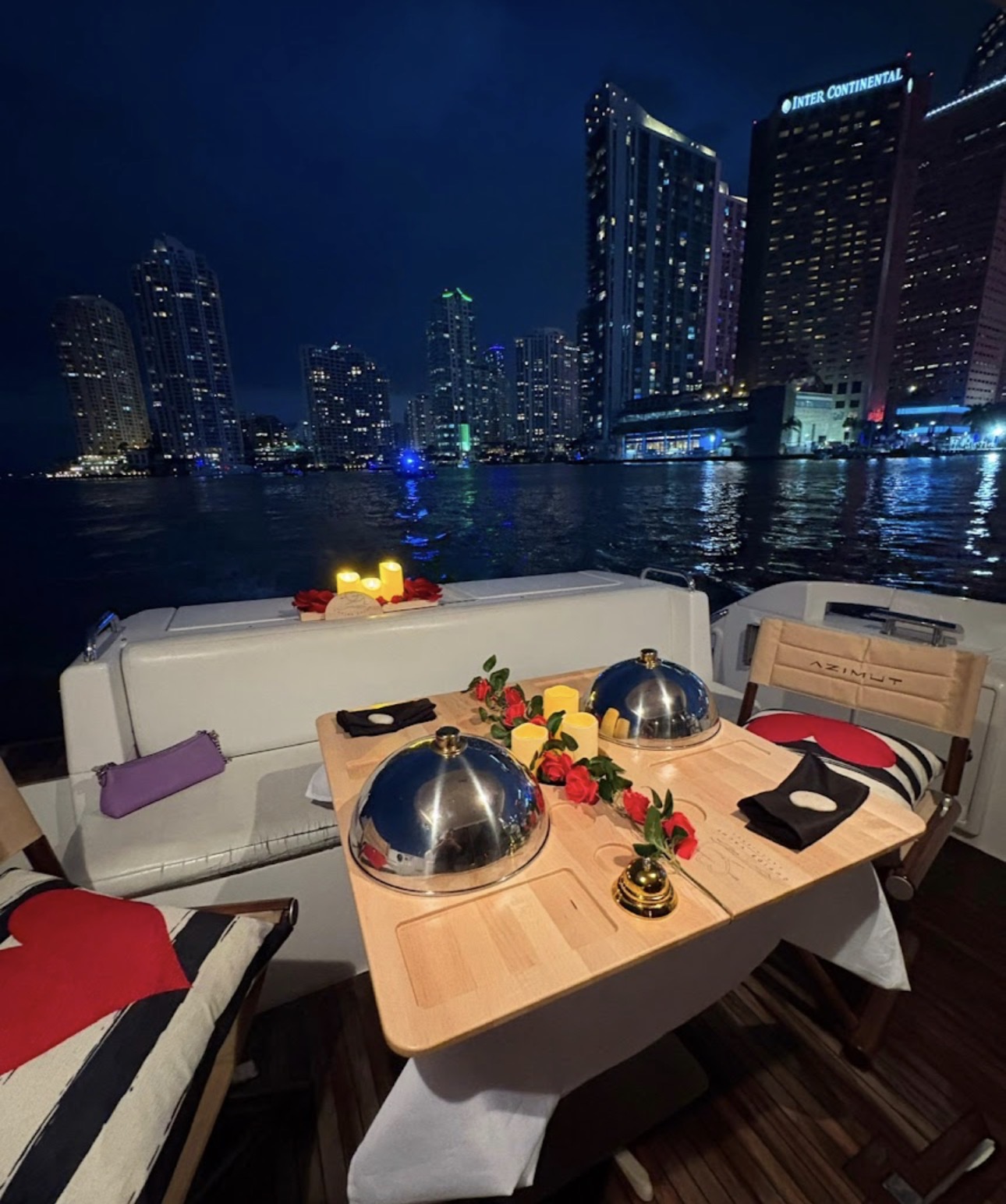 Candlelit dinner table set for two on board with the Miami skyline at night